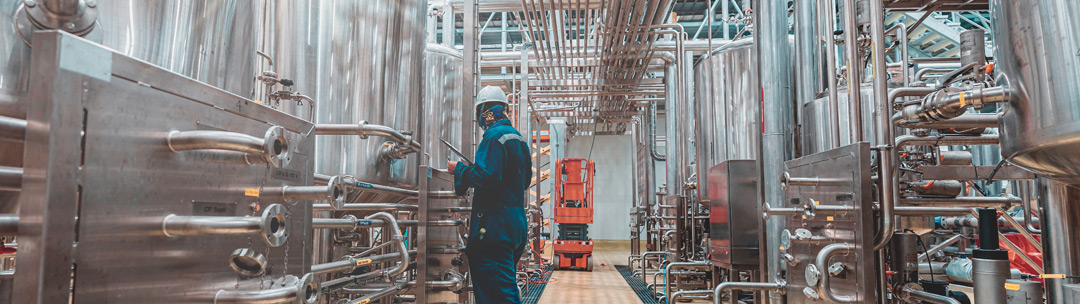 Worker examining equipment among stainless steel tanks and piping in an industrial processing facility